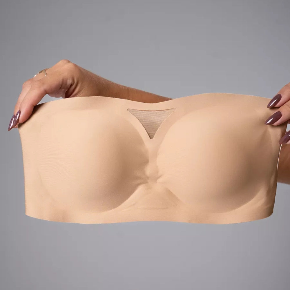 Imagem do Sutiã Tomara que Caia Sensação na cor bege, sendo segurado por duas mãos, evidenciando sua modelagem flexível e estruturada. O design sem alças conta com um recorte triangular em tule no centro, proporcionando elegância e sustentação natural.