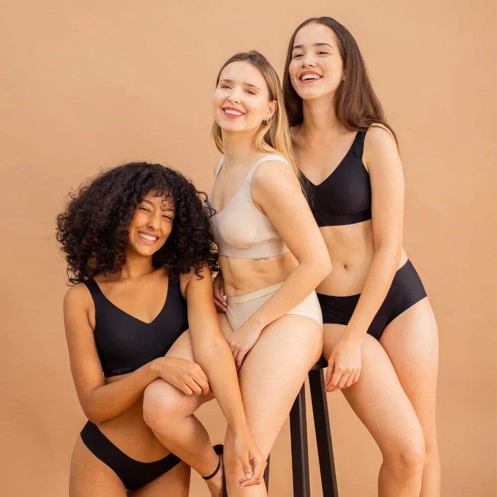 Três mulheres sorridentes vestindo o Sutiã Curves Cygnuss em preto e bege, transmitindo diversidade, elegância e autoconfiança.