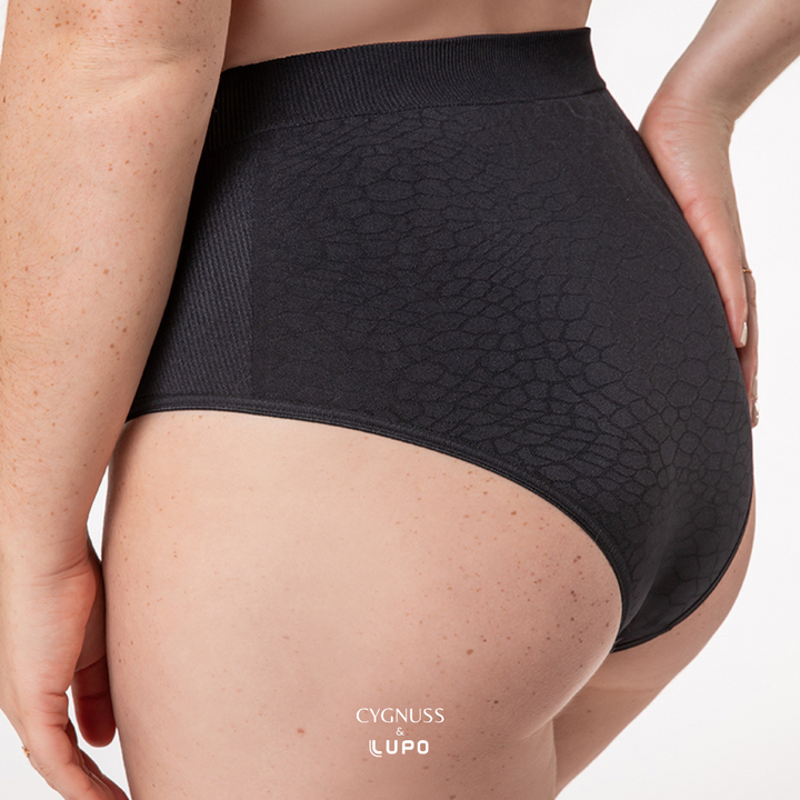 Close-up lateral de uma mulher usando uma calcinha modeladora preta de cintura alta. O tecido texturizado sem costuras apresenta um design elegante, com áreas estratégicas de compressão suave para modelar a silhueta. A cintura elástica garante ajuste confortável, enquanto o material respirável proporciona frescor ao longo do dia. O logotipo da Cygnuss & Lupo está sobreposto na parte inferior da peça.