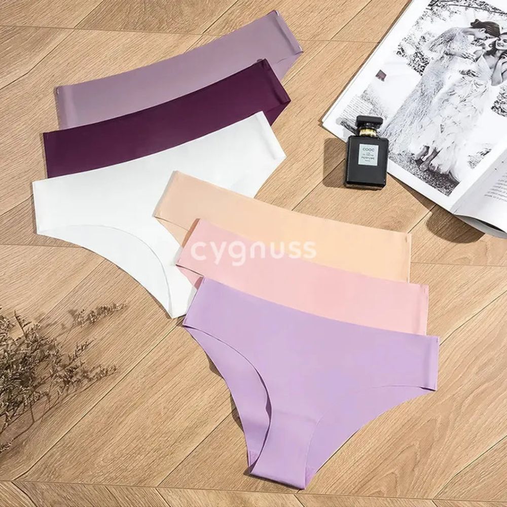 Imagem de calcinhas sem costura da Cygnuss dispostas em um fundo de madeira, apresentando cores suaves e elegantes, incluindo lilás, roxo, branco, rosa e bege. Ao lado, um perfume e uma revista complementam a composição sofisticada.