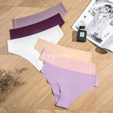 Imagem de calcinhas sem costura da Cygnuss dispostas em um fundo de madeira, apresentando cores suaves e elegantes, incluindo lilás, roxo, branco, rosa e bege. Ao lado, um perfume e uma revista complementam a composição sofisticada.