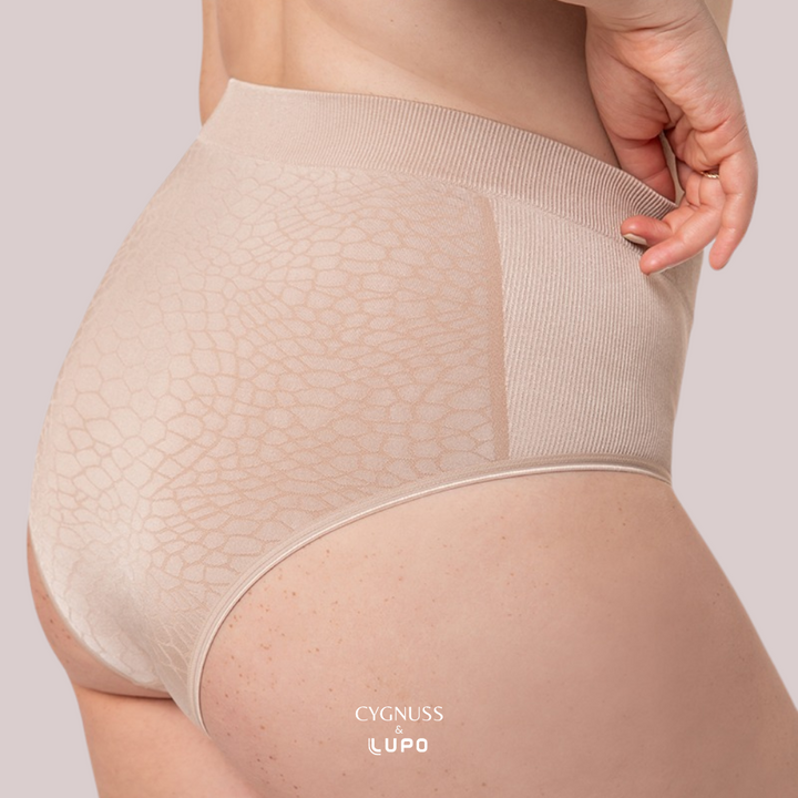 Close-up lateral de uma mulher usando uma calcinha modeladora nude de cintura alta. O tecido texturizado possui um design elegante com detalhes que criam um efeito modelador suave. A cintura elástica ajusta-se perfeitamente ao corpo, proporcionando conforto e sustentação. O logotipo da Cygnuss & Lupo está sobreposto na parte inferior da peça. Fundo nude rosado. 