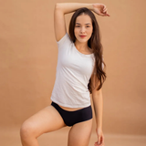 Mulher posando com uma camiseta branca e calcinha preta sem costura da Cygnuss. Com um fundo em tom terroso, a imagem destaca o ajuste confortável e a elegância discreta da peça.