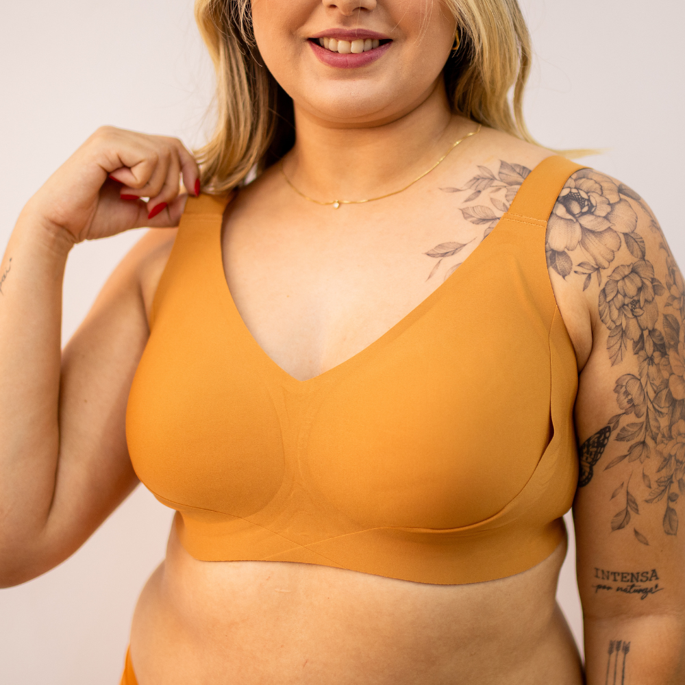 Mulher loira com tatuagem floral no ombro veste o Sutiã Curves Cygnuss na cor laranja, 
