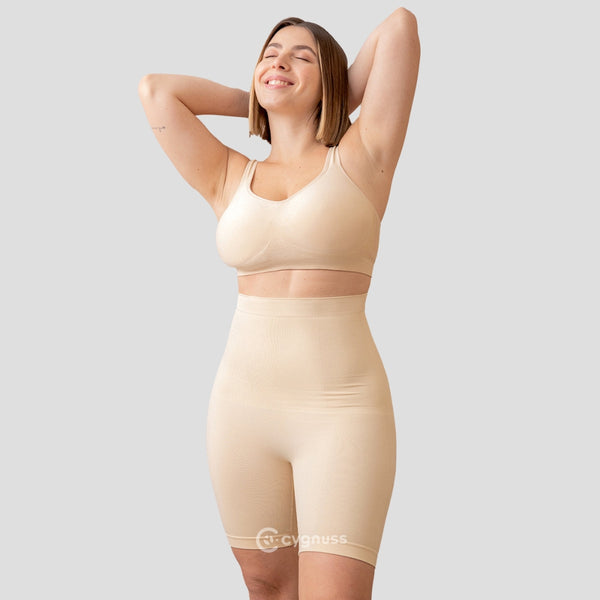 Mulher sorridente, de pé, usando o Short Premium Modelador com Faixas de Silicone na cor bege. O modelador proporciona um contorno perfeito ao corpo, com alta elasticidade e conforto, destacando a silhueta de forma elegante.