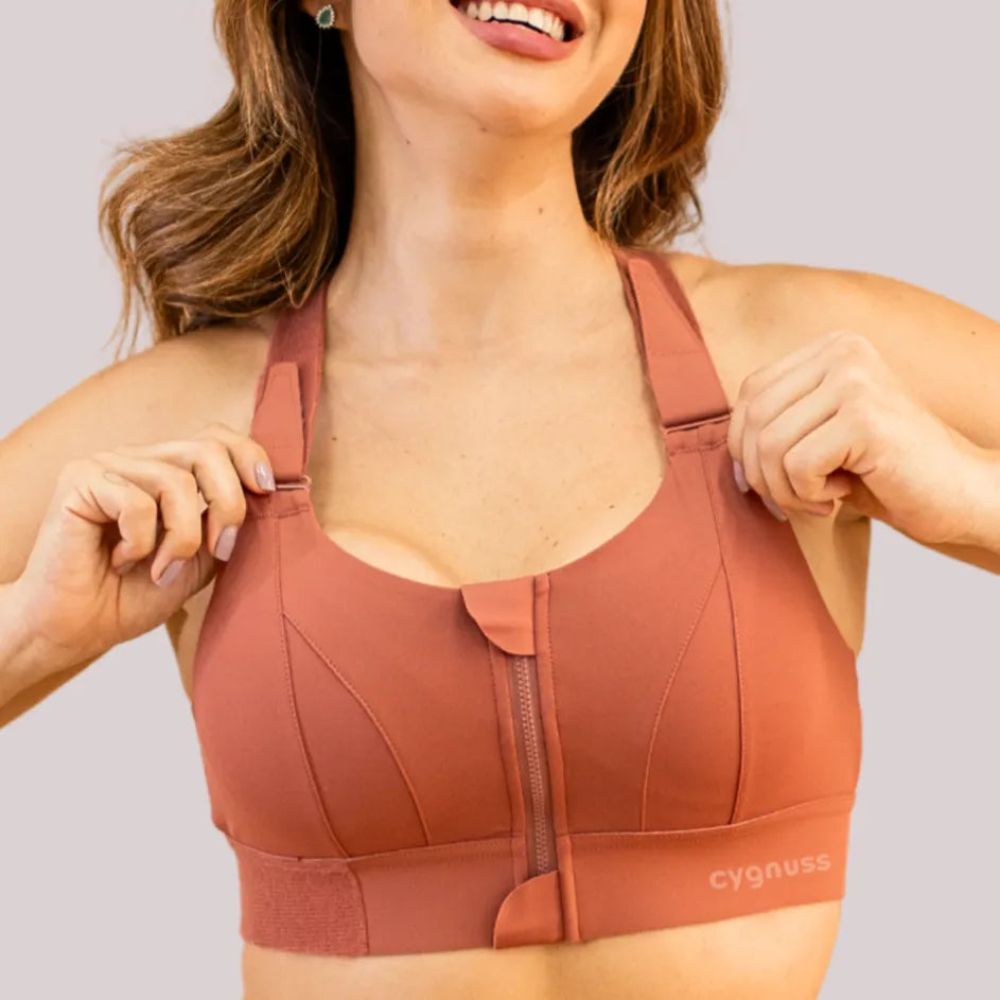 Mulher vestindo o sutiã esportivo com zíper frontal da Cygnuss, em tom terroso, ajustando as alças reguláveis para melhor suporte e conforto durante a prática de atividades físicas
