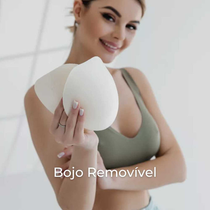 Mulher sorridente vestindo o Sutiã FIT verde oliva com alça fina. Ela segura dois bojos removíveis nas mãos, destacando a versatilidade do produto. A imagem traz a legenda “Bojo Removível”, reforçando essa funcionalidade.