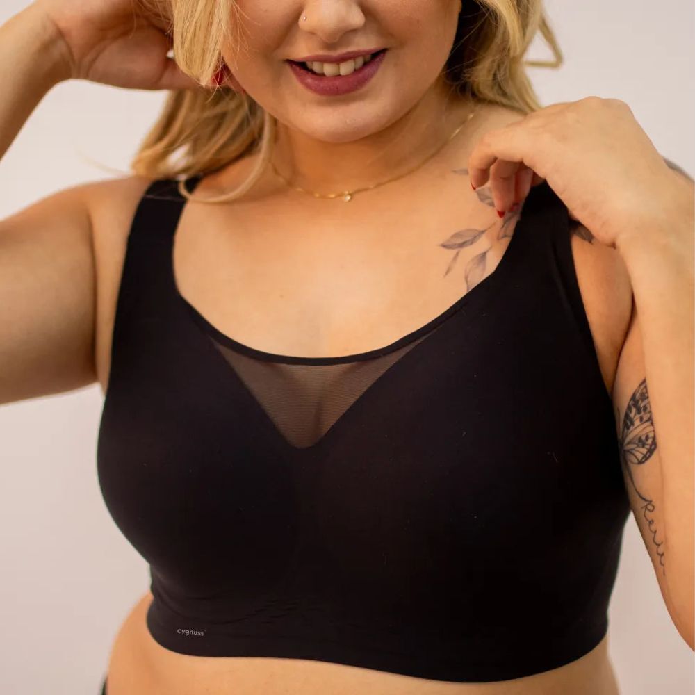 Mulher sorridente vestindo o sutiã preto Cygnuss, destacando o design sem costuras, alças largas e o detalhe em tule no decote para um toque moderno e sofisticado.