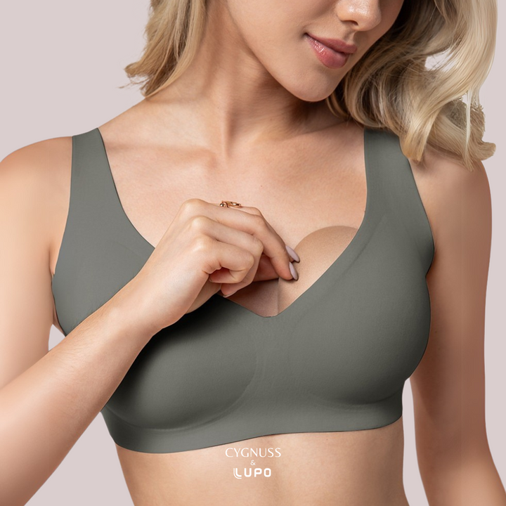 Mulher vestindo um sutiã sem costura em tom acinzentado, demonstrando o bojo removível do modelo. O design anatômico proporciona ajuste confortável e suporte natural. O logotipo da Cygnuss & Lupo está visível na parte inferior da peça.