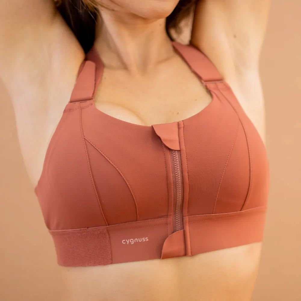  Detalhe do sutiã esportivo Cygnuss na cor terracota, evidenciando o fecho frontal com zíper e aba protetora para maior conforto e praticidade no uso