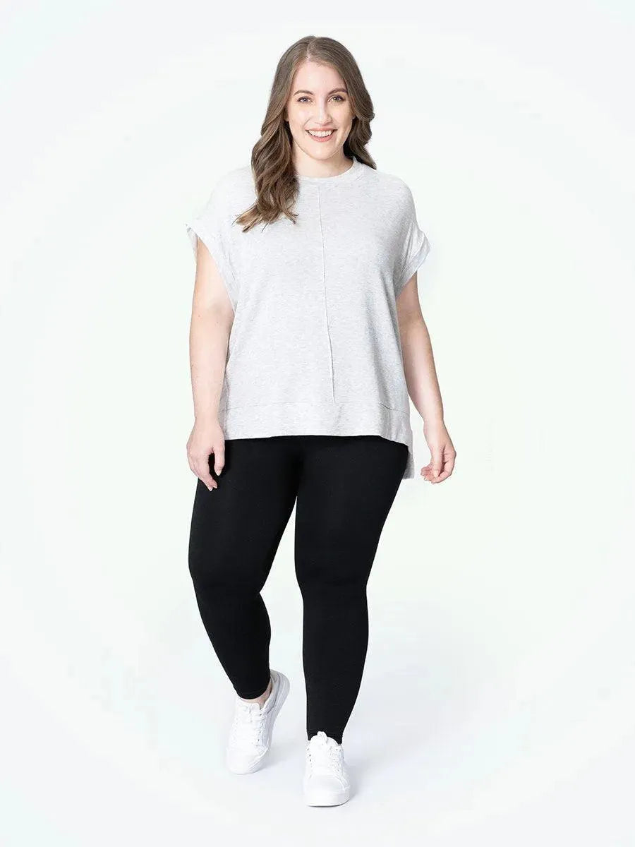 Mulher plus size sorrindo, usando a Legging Jade Fit Modeladora de Cós Alto na cor preta, combinada com camiseta cinza e tênis branco, destacando o conforto e o estilo da peça no visual casual.

