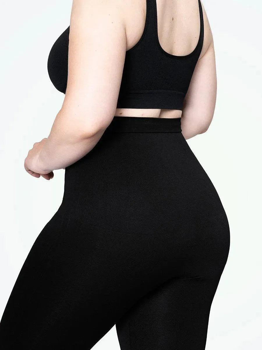 Mulher plus size usando a Legging Jade Fit Modeladora de Cós Alto na cor preta, destacando o cós alto que modela a região abdominal e a compressão que valoriza as curvas, em uma pose lateral.