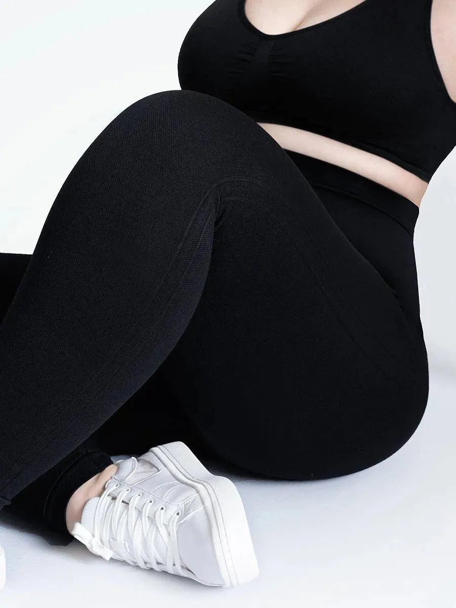 Detalhe da Legging Jade Fit Modeladora de Cós Alto na cor preta, em vista lateral com foco no tecido, destacando a compressão suave e o ajuste perfeito, combinada com tênis branco e top preto.