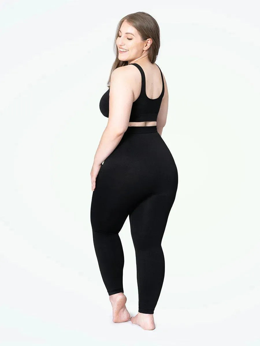 Mulher plus size sorrindo, usando a Legging Jade Fit Modeladora de Cós Alto na cor preta, combinada com top preto, em pose de costas que destaca o cós alto e o efeito modelador na região abdominal e nas pernas.