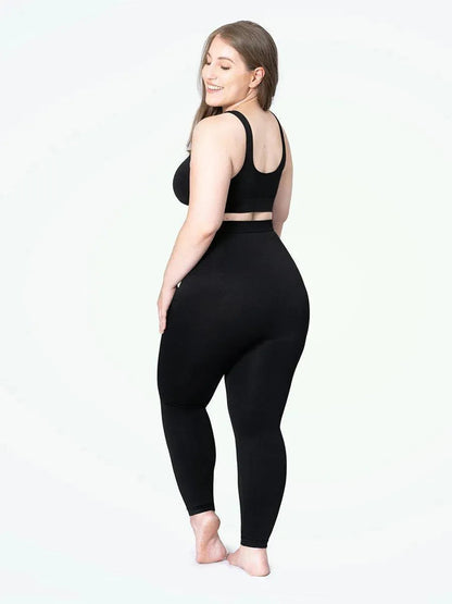 Mulher plus size sorrindo, usando a Legging Jade Fit Modeladora de Cós Alto na cor preta, combinada com top preto, em pose de costas que destaca o cós alto e o efeito modelador na região abdominal e nas pernas.